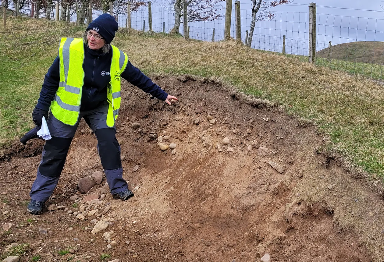 BGS Marine Geoscientist Margaret Stewart describes the till and topsoil overlying the bedrock-cut meltwater channels at Carlops, a classic example of a subglacial drainage system. BGS © UKRI.