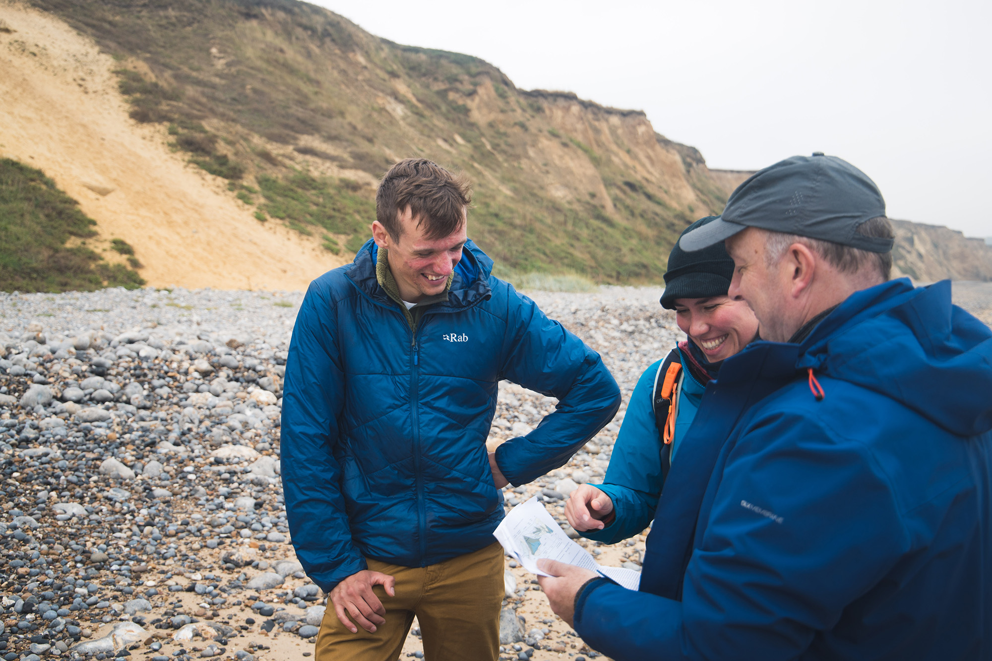 Three happy people looking at a piece of paper with a beach and a sandy cliff in the background